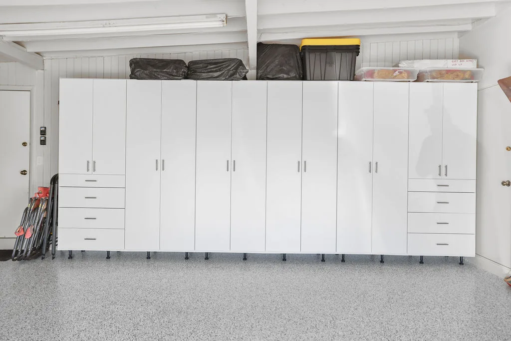 Custom white garage cabinet system with overhead and base storage over a speckled epoxy floor