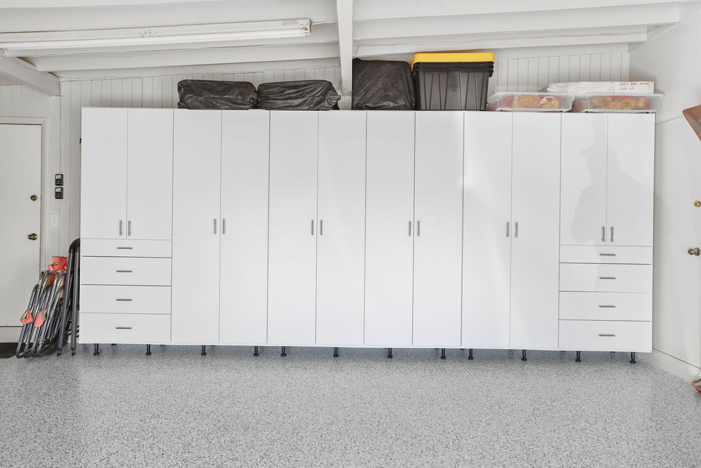 Clean white custom garage cabinet system with drawers along a wall over a speckled epoxy floor