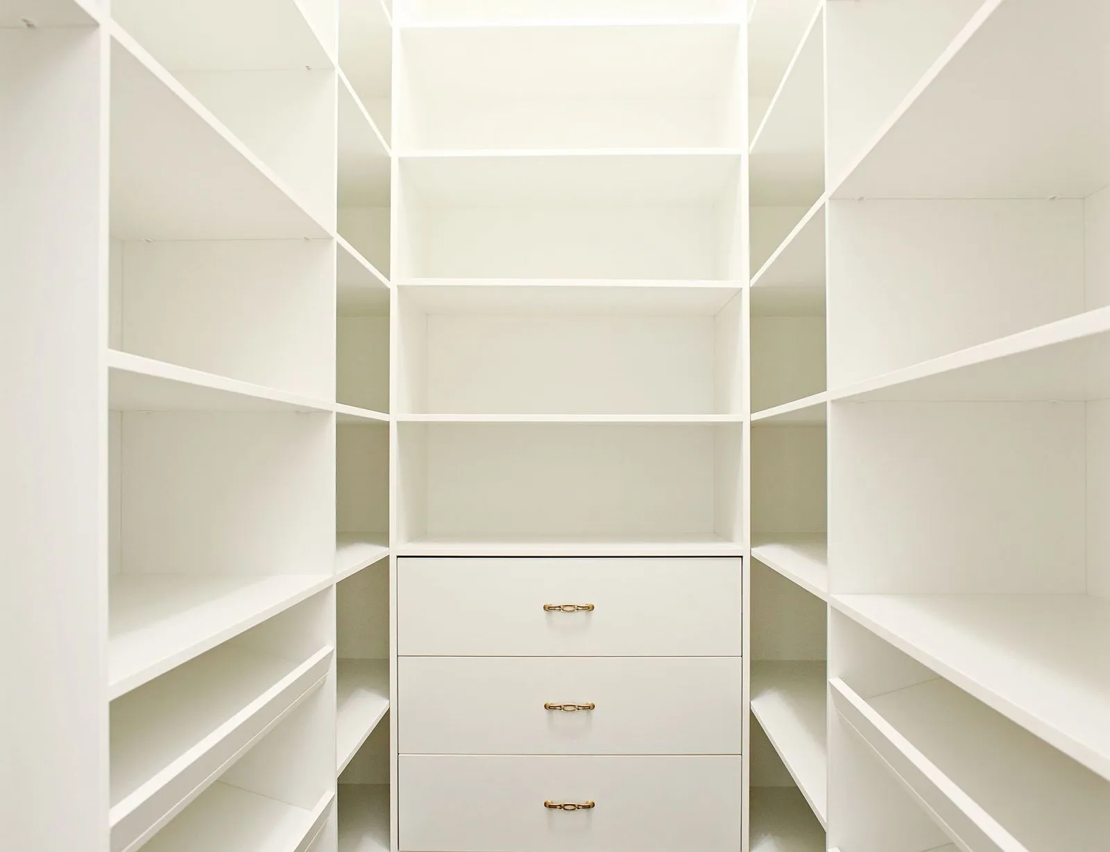 White custom-built reach-in closet with adjustable shelving and warm brass cup-pull drawers