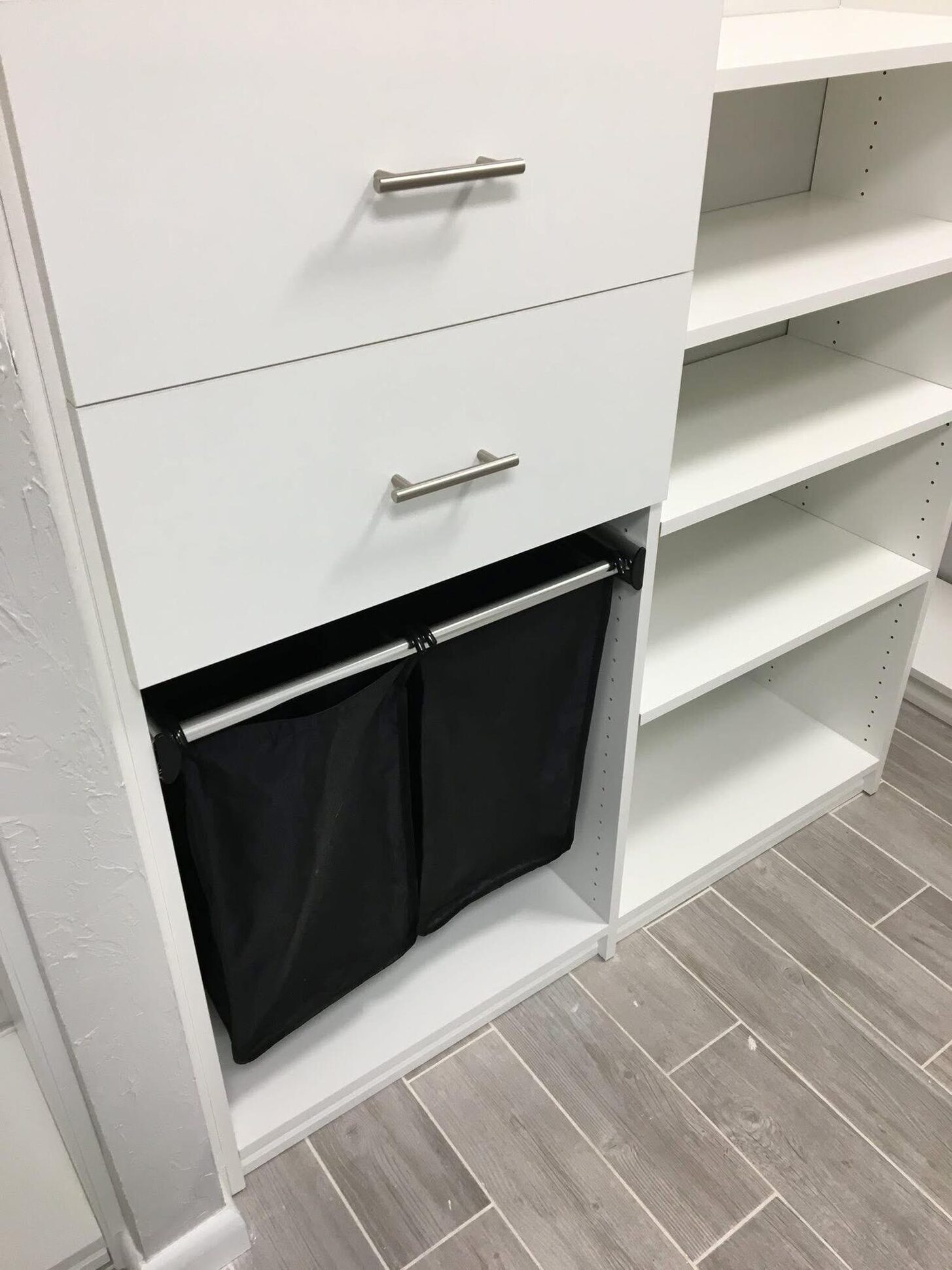 Integrated pull-out laundry hamper built into custom white closet shelving