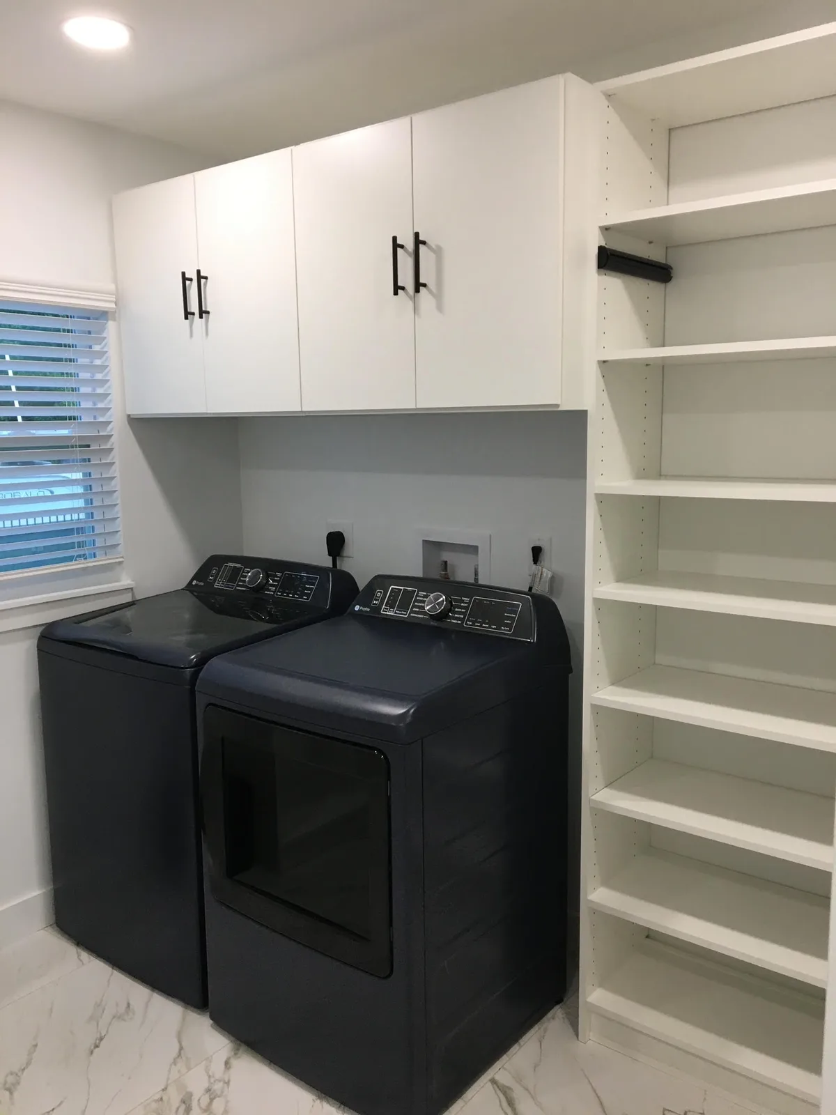 Custom laundry room with white cabinetry, hanging space, and open shelving beside the washer and dryer