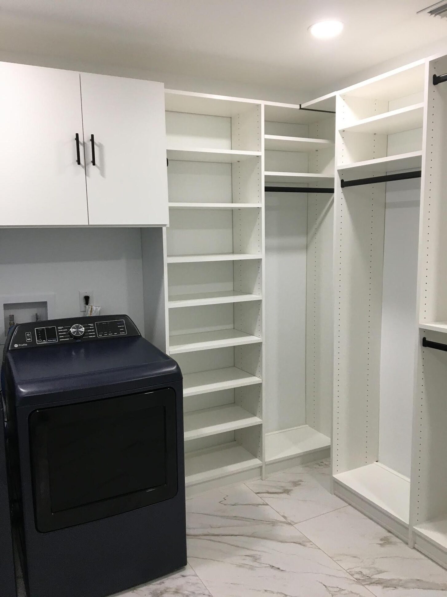 Custom laundry and utility closet with corner shelving and a navy dryer on marble-look tile