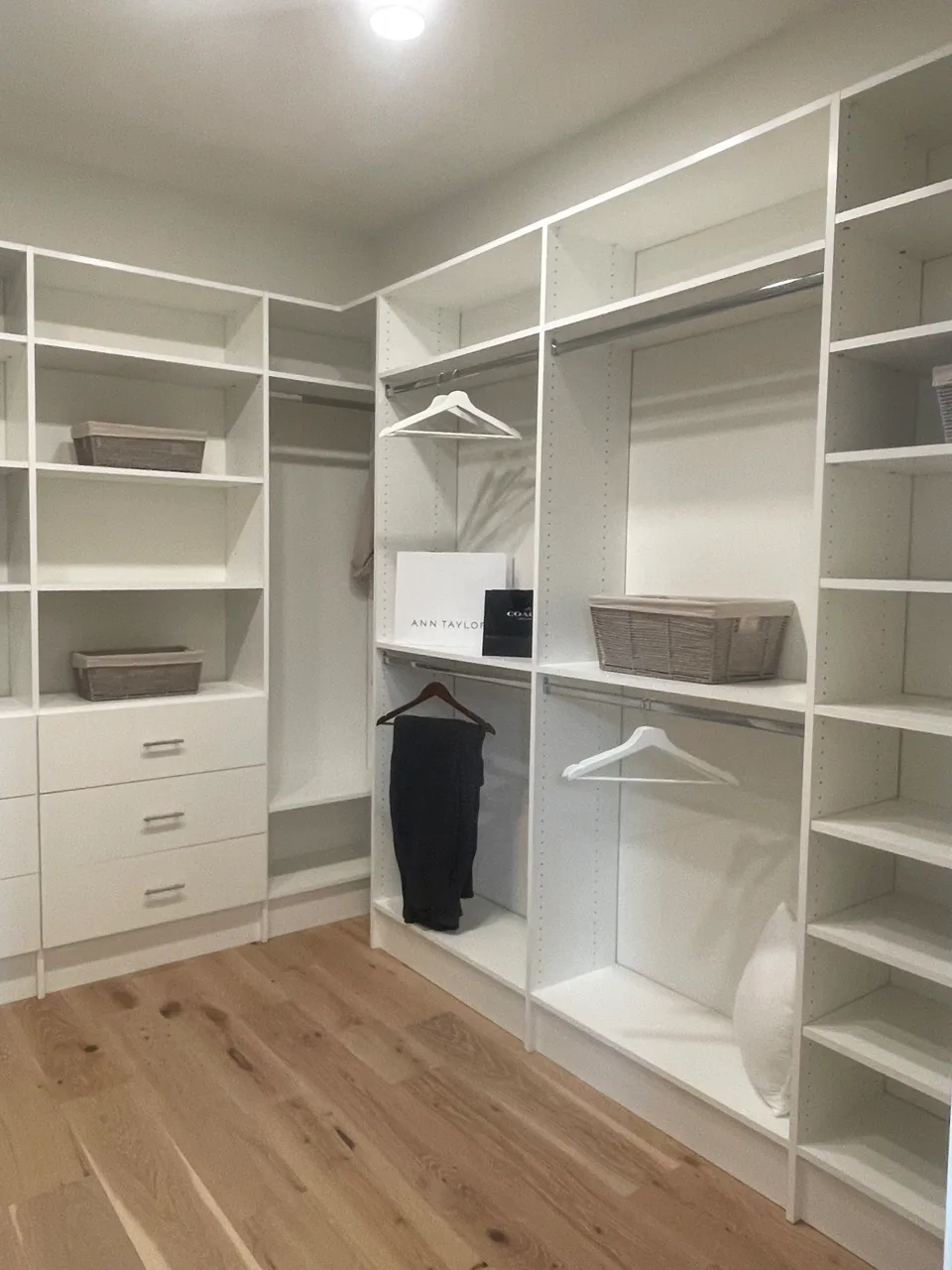 Bright custom walk-in closet with white perimeter shelving over wood-look flooring